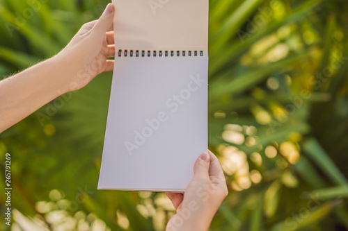 Women's hands in a tropical background holding a signboard, drawing block, paper, mockup