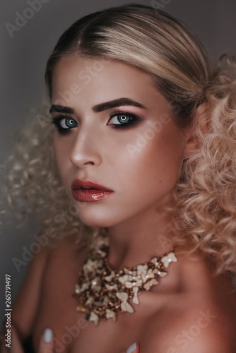 Beautiful blonde girl with bright artistic make-up and beautiful hair in a beige dress with corals on the background