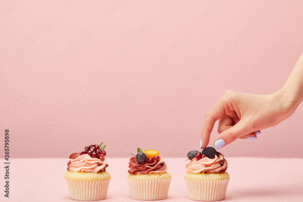cropped view of woman with sweet cupcakes with fruits and berries isolated on pink