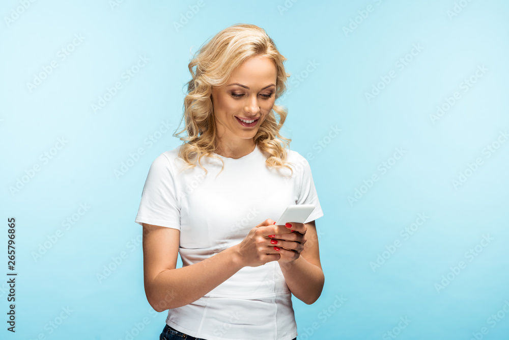 cheerful blonde woman using smartphone and standing on blue cheerful blonde woman using smartphone and standing on blue