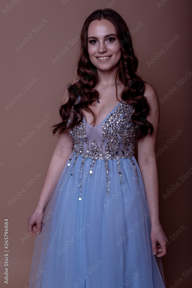 Beautiful young girl in a flying blue dress with sequins and embroidery. Flowing fabric. bride in a white dress on a beige background. gorgeous brunette on a studio background. Isolate.girl on a brown Beautiful young girl in a flying blue dress with sequins and embroidery. Flowing fabric. bride in a white dress on a beige background. gorgeous brunette on a studio background. Isolate.girl on a brown