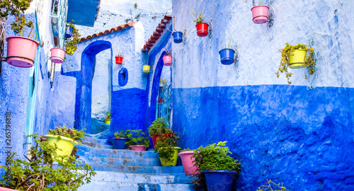 Beautiful blue walls with bright doors and colorful flower pots on the walls on a sunny day, Chefchaouen city medina in Morocco. Panorama © olenatur