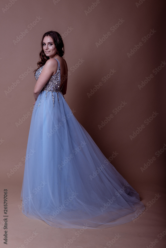Beautiful young girl in a flying blue dress with sequins and embroidery. Flowing fabric. bride in a white dress on a beige background. gorgeous brunette on a studio background. Isolate.girl on a brown Beautiful young girl in a flying blue dress with sequins and embroidery. Flowing fabric. bride in a white dress on a beige background. gorgeous brunette on a studio background. Isolate.girl on a brown