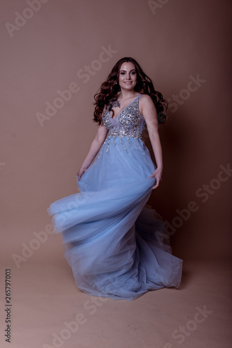 Beautiful young girl in a flying blue dress with sequins and embroidery. Flowing fabric. bride in a white dress on a beige background. gorgeous brunette on a studio background. Isolate.girl on a brown © Tanya