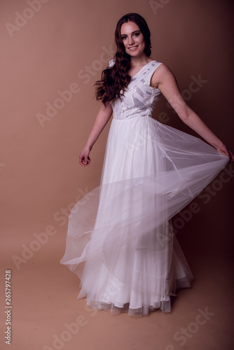 Beautiful young girl in a flying white dress. Flowing fabric. bride in white dress on beige background. gorgeous brunette on a studio background. Isolate