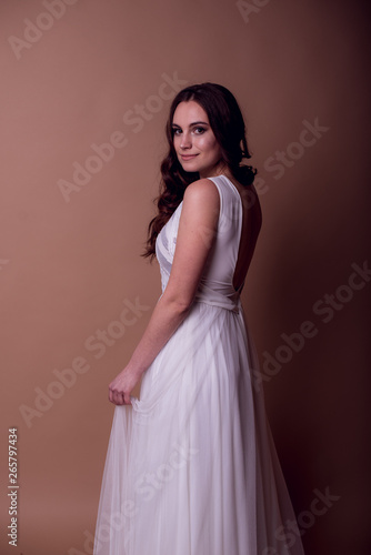  Beautiful young girl in a flying white dress. Flowing fabric. bride in white dress on beige background. gorgeous brunette on a studio background. Isolate