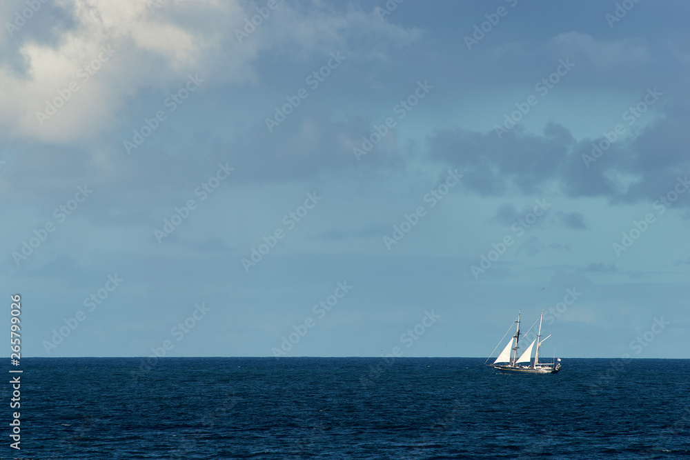 A large blue sailing boat with white sails, making it's way up the east coast of Australia on the Pacific Ocean; deep blue sea and a lightly cloudy blue sky. A large blue sailing boat with white sails, making it's way up the east coast of Australia on the Pacific Ocean; deep blue sea and a lightly cloudy blue sky.
