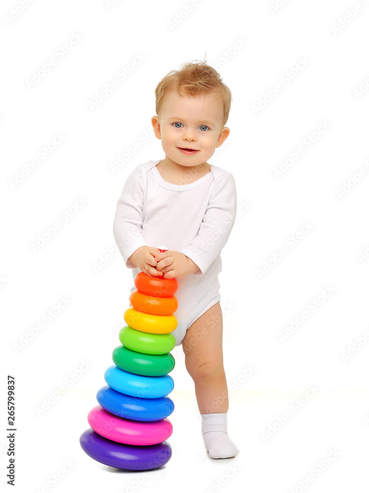 A child of 11 months in a white body is on a white background and holds a bright colored toy-pyramid