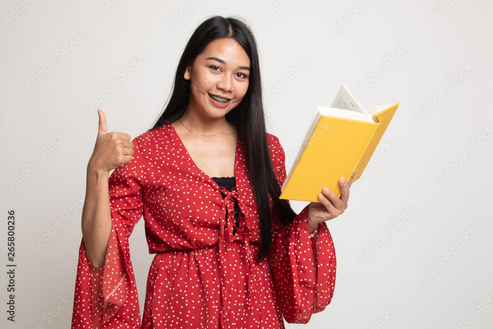 Young Asian woman thumbs up with a book. Young Asian woman thumbs up with a book.
