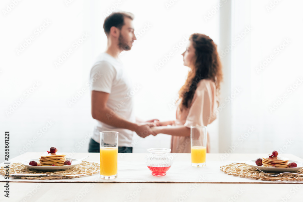 selective focus of couple holding hands with pancakes and orange juice on foreground