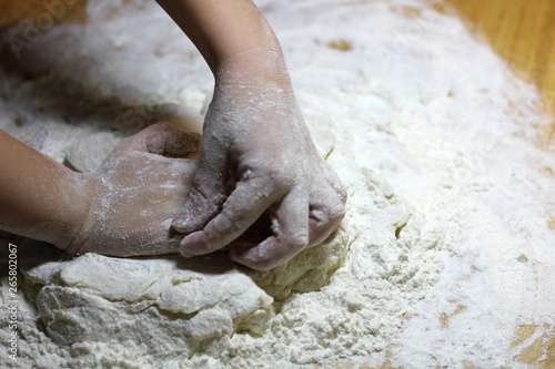 Children's hands and dough. Little boy kneading a dough. Healthy handmade food concept. bakery products, pizza, flour. cooking workshop. baby's hands roll out a dough on a wooden table.