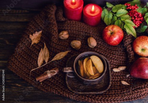 Autumn, fall leaves, hot cup of tea, knitted blanket, red berries, candles on wooden table background. Seasonal, autumnal hot drink. Autumn relaxing and still life concept. Toned image. Top view.