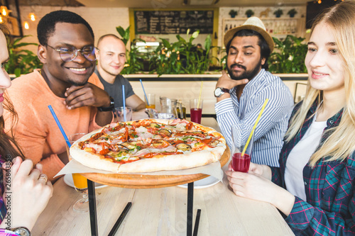 A company of multicultural  young people in a cafe eating pizza  drinking cocktails  having fun