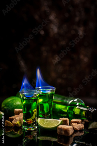 absinthe poured shots with lime slices and sugar on dark table background photo