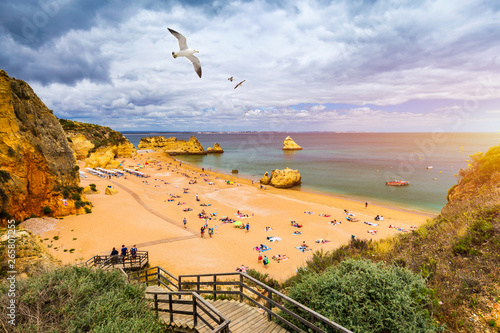 Wooden walkway to famous Praia Dona Ana beach with turquoise sea water and cliffs, flying seagulls over the beach, Portugal. Beautiful Dona Ana Beach (Praia Dona Ana) in Lagos, Algarve, Portugal.