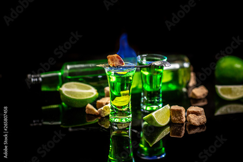 absinthe shots with sugar cubes. absinthe poured into a glass. bottle of absinthe with brown sugar and lime isolated on black background. space for text