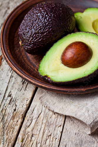 Fresh organic avocado on ceramic plate and linen napkin on rustic wooden table background.