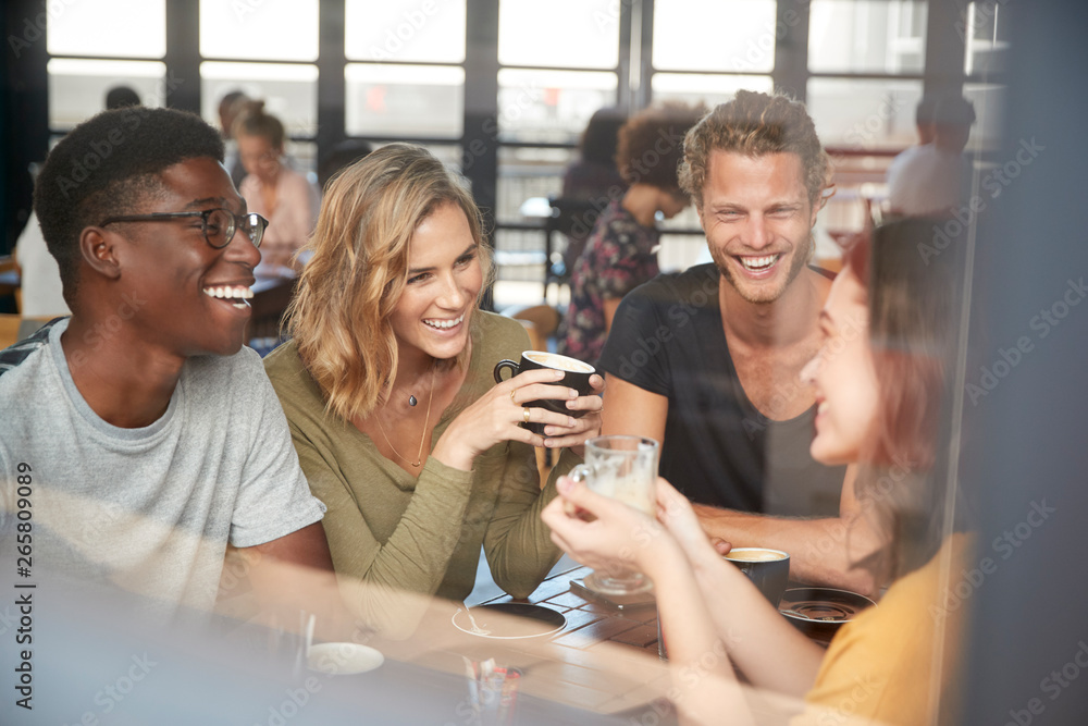 Group Of Friends Sitting At Table In Busy Coffee Shop Talking Group Of Friends Sitting At Table In Busy Coffee Shop Talking