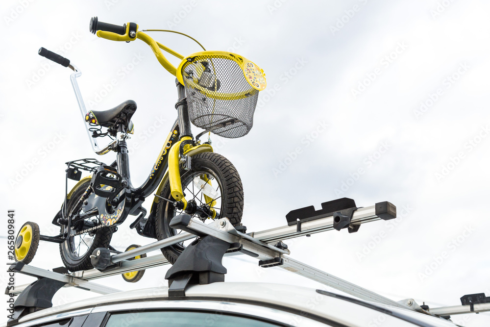 Bicycle transport - a children's bicycle on the roof of a car against the sky in a special mount for cycling. The decision to transport large loads and travel by car Bicycle transport - a children's bicycle on the roof of a car against the sky in a special mount for cycling. The decision to transport large loads and travel by car
