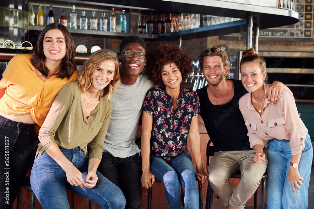 Obraz premium Portrait Of Male And Female Friends Sitting By Counter In Sports Bar