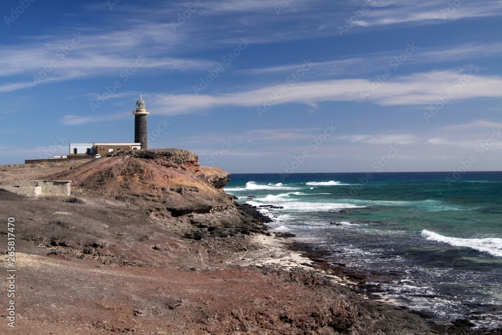 Lighthouse in barren landscape with wild blue sea at north-west tip of Fuerteventura, Canary Islands
