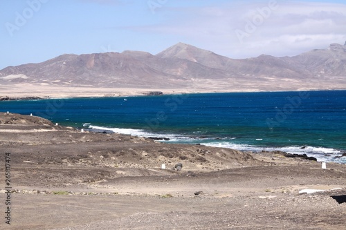 Blue lagoon surrounded by dry bare sand dunes at north-west coast of Fuerteventura, Canary Islands