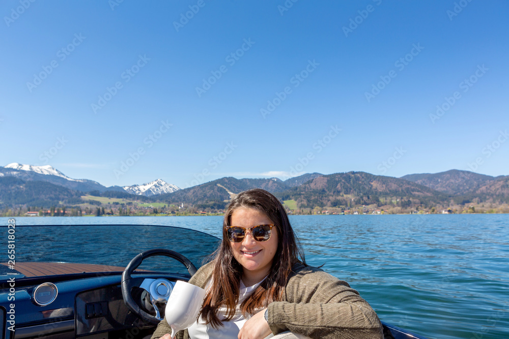 Young latin lady poses at the wheelof a motor boat while on lake