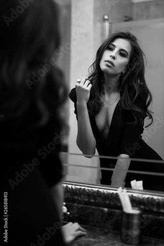 Cinematic black and white portrait of sexy brunette woman in little black dress looking in the mirror. Noir, sensual, italian