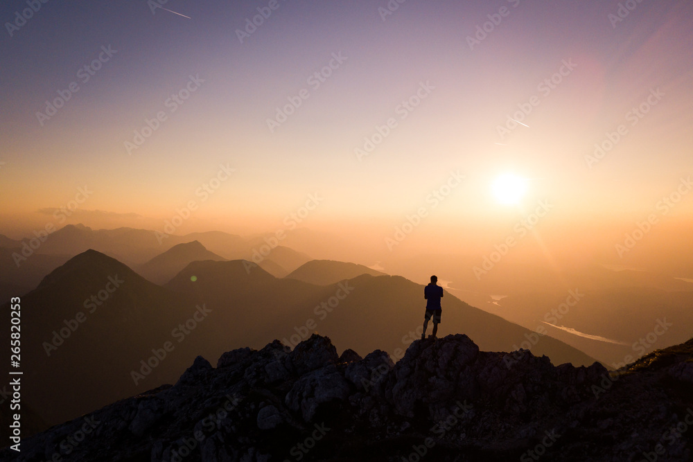 Man standing on the top of a mountain and looking down- hiking silhouette