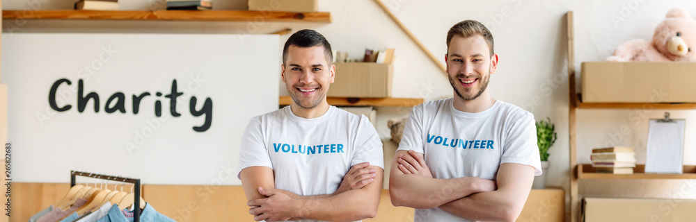 Obraz premium panoramic shot of handsome volunteers standing with crossed hands near placard with charity inscription