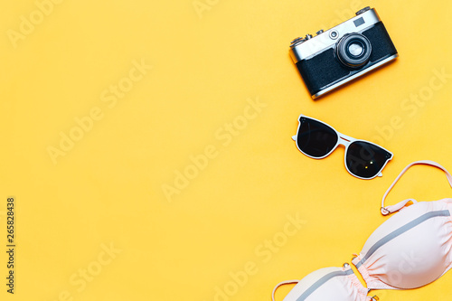 Summer accessories concept on yellow background, flatlay, copyspace, vintage camera, white sunglasses and swimsuit