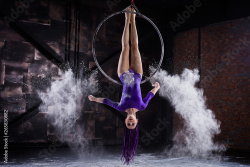 A young  slender girl in a lavender leotard and lilac dreads  doing gymnastics on the air ring  the Hoop and throws the hands of the white powder in the form of a cloud.