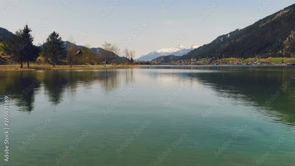 Flight of the camera over mountain lake with the transfer of the perspective on the panorama of snow-capped mountains. Wild nature. Sunny day. Flight of the camera over mountain lake with the transfer of the perspective on the panorama of snow-capped mountains. Wild nature. Sunny day.