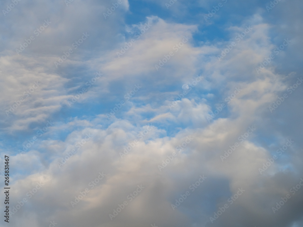 Moon in blue sky seen through cloudscape