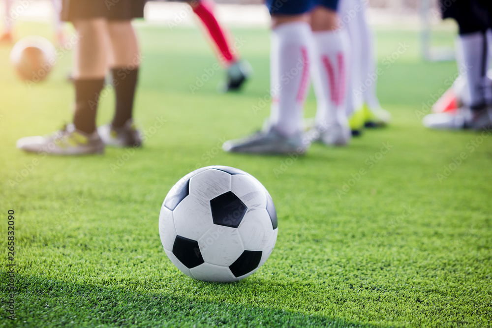 soccer ball on green artificial turf with blurry soccer players standing