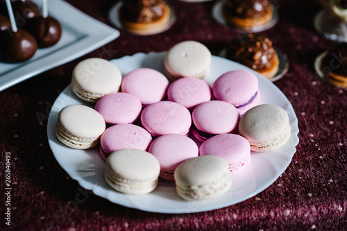 Delicious sweet pink, purple, pastel, beige macaroons in a plate on a violet background. Festive sweet table with baking.