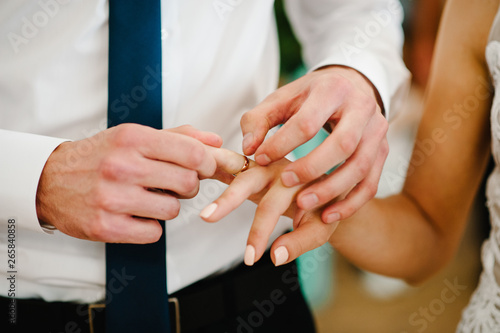 The bride s hand wears an engagement gold ring on the groom s finger. Wedding day. Hands with wedding rings. Close up.