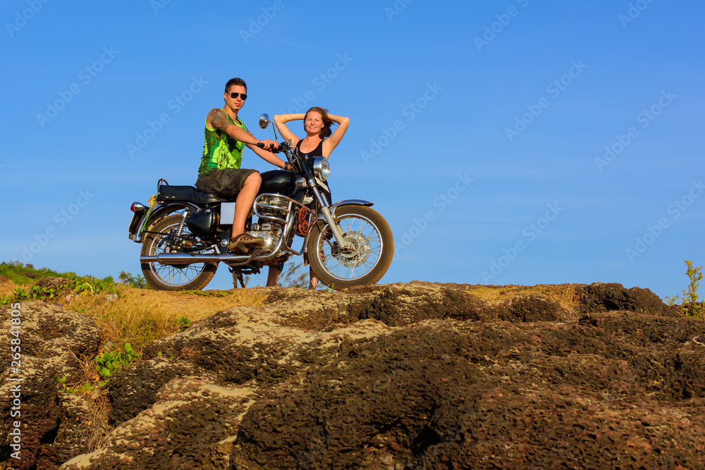 Obraz premium Young couple on a motorcycle on on rocky ground. Happy guy and girl travelling on a motorbike.
