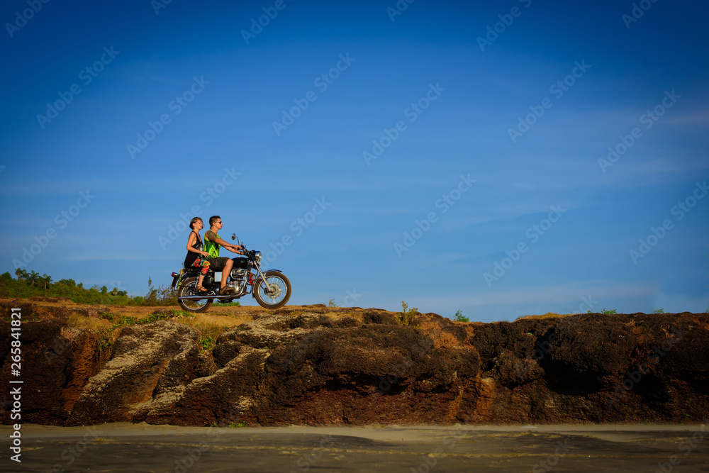 Naklejka premium Young couple on a motorcycle on on rocky ground. Happy guy and girl travelling on a motorbike.