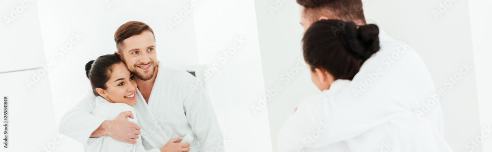 panoramic shot of happy man hugging attractive woman while looking at mirror panoramic shot of happy man hugging attractive woman while looking at mirror