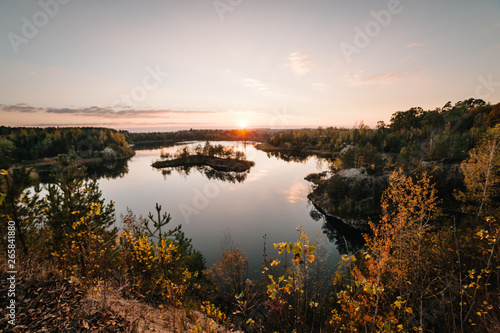 Sunset on lake, landscape. Autumn nature. Island for fishing in the middle of the lake. Colorful sky and water in lake reflected in evening.