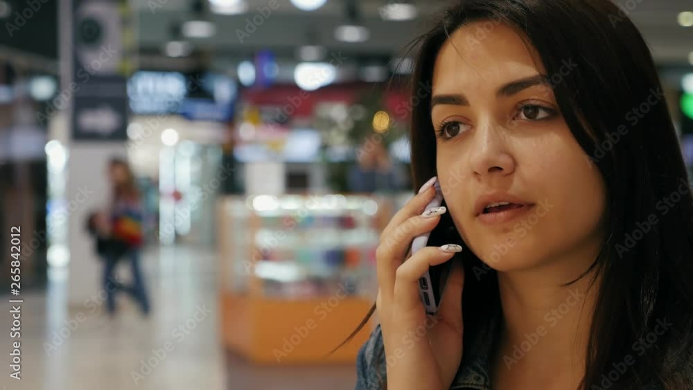 Beautiful woman in jeans jacket sitting on the bench in the mall talking with friend on the phone Beautiful woman in jeans jacket sitting on the bench in the mall talking with friend on the phone