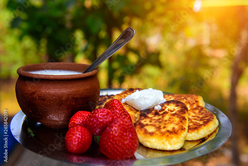 Curd fritters with sour cream and strawberries, homemade traditional Ukrainian and Russian syrniki on on blurred green background.