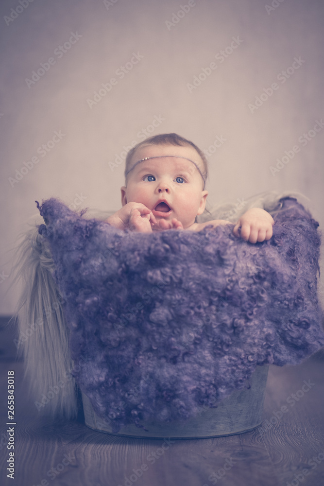 Fototapeta premium Portrait Baby sitzt im Eimer Hände Füße Fell lila vintage