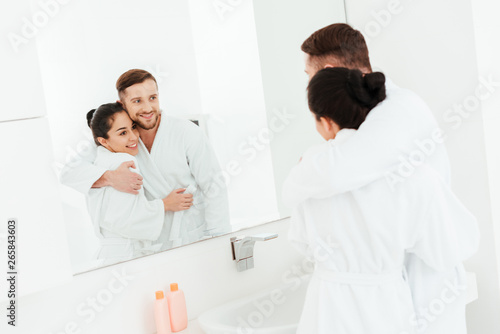 selective focus of happy man hugging attractive brunette woman while looking at mirror