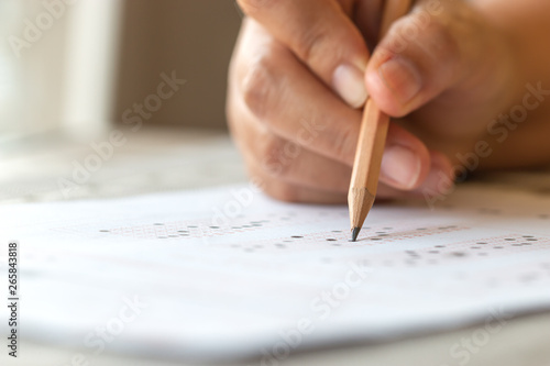 Exam test school or university concept : Hand student holding pencil writing standardized answer multiple carbon paper form with gray black answers sheet bubbled of question in examination assessment. photo