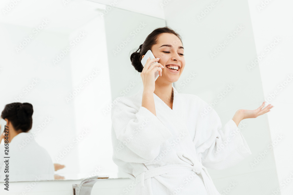 low angle view of happy young woman gesturing while talking on smartphone in bathroom low angle view of happy young woman gesturing while talking on smartphone in bathroom