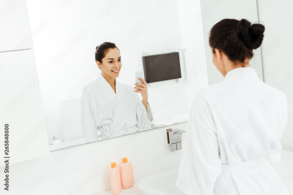 selective focus of attractive and cheerful young woman taking photo in bathroom