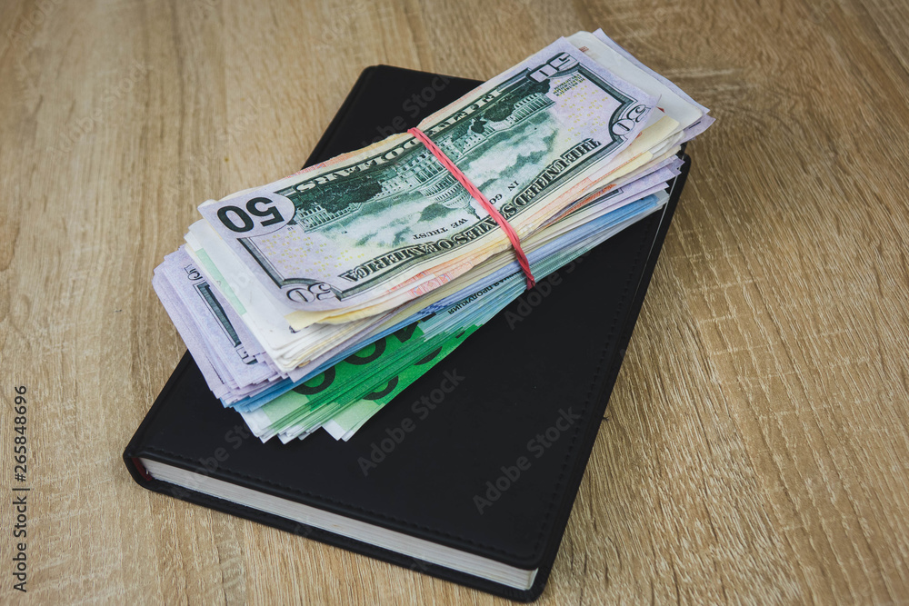 American dollars, euros, rubles are on a black notebook. The concept of a financial plan for the year, investment or saving money. wooden background American dollars, euros, rubles are on a black notebook. The concept of a financial plan for the year, investment or saving money. wooden background