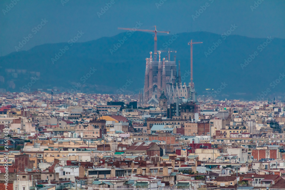 Aerial view of the Barcelona city with the Temple Expiatori de la Sagrada Familia (Expiatory Church of the Holy Family) in the distance on the background of mountains at twilight, Spain
